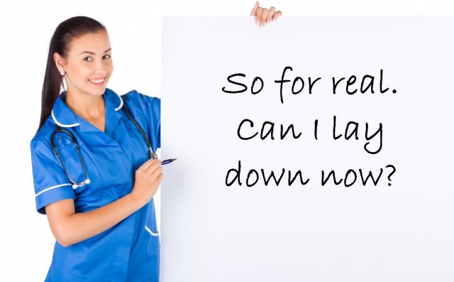 A nurse in blue scrubs stands holding a white card in her right hand. Her left hand is holding a marker posed over the card. The card reads, "So for real. Can I lay down now?"