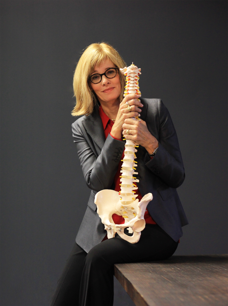 Photo of Cathryn Jakobson Ramin. She is wearing a black jacket and holding a medical model of a human spine.