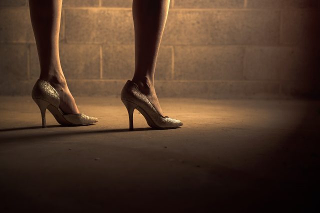 A woman is standing on a concrete floor wearing stilettos. Only her calves and feet are shown. She is not wearing socks.