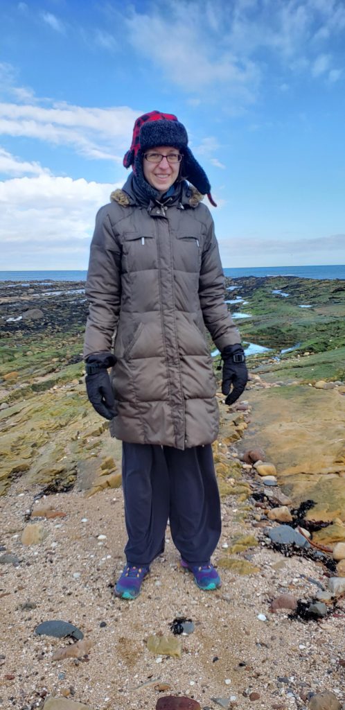 A photo of me bundled up in a thick winter hat and coat...while standing on a beach. Hey, it was March in Scotland, and it was still pretty cold.