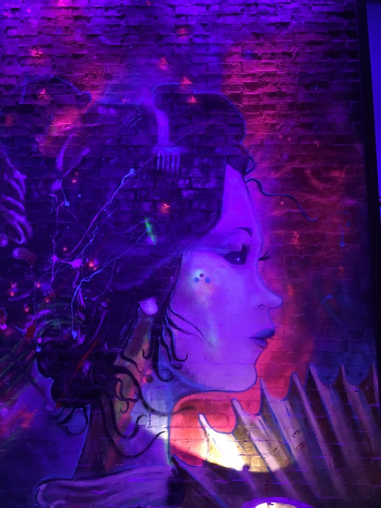 A mural of a young Asian woman under ultraviolet lights.