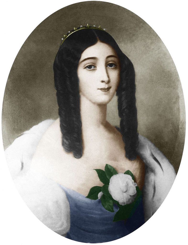 A portrait of Marie Duplessis by Édouard Viénot. She has a tiara on top of her dark curls. Her face is heart-shaped, and her shoulders appear rounded. She's wearing some sort of white shawl and a blue dress. A white flower is pinned to her front. 