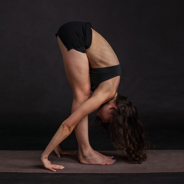 A woman in a sports bra and underwear leans into a deep forward bend. This is definitely an example of spinal flexion, which is not comfortable for people with herniated discs.