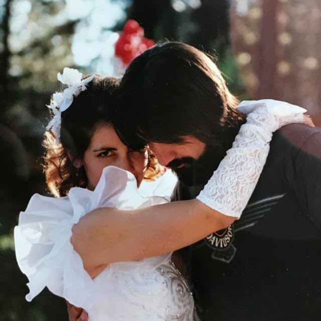 A wedding photo of Lisa and her second husband, taken in 1990. Both their faces are obscured; he's looking down, and her puffy sleeve covers the bottom half of her face. Lisa is wearing white gloves, and has her arms wrapped around her new husband.