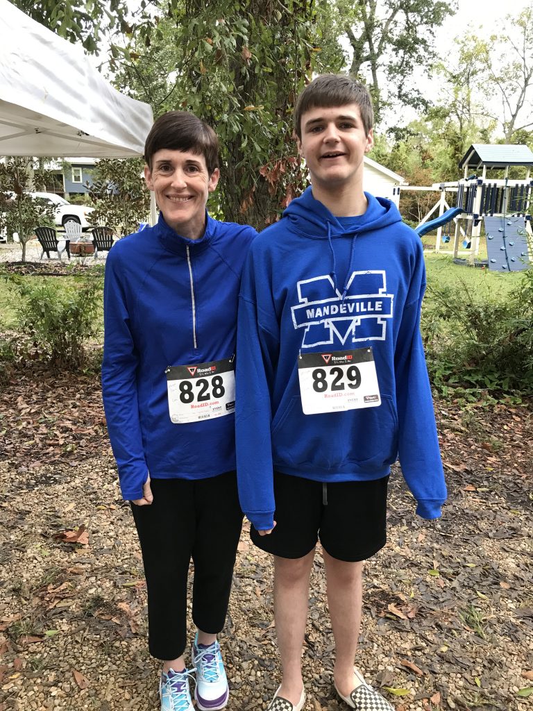 Claire and her older son are outside before a race. They both have race numbers pinned to the front of their blue sweatshirts.