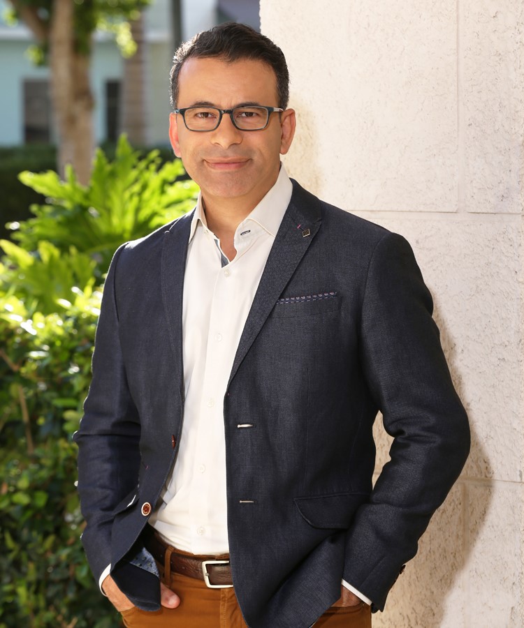 A publicity photo of Dr. Makary. He's wearing thick, rectangular, nerd-style glasses, a blazer, a white button-up shirt, and dark orange pants. He looks like an Egyptian Fred Armisen.