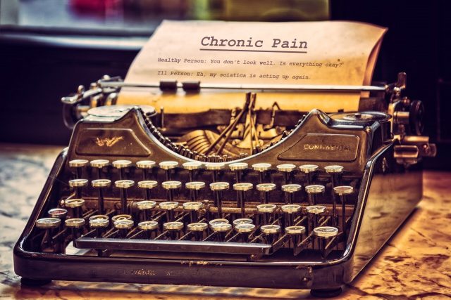 A sepia-toned photo of an old-fashioned typewriter. There's a piece of paper sticking out of the top. It's a script, and the heading reads, "Chronic Pain." Underneath is written, "Healthy Person: You don't look well. Is everything okay?" "Sick Person: Eh, my sciatica is acting up again." That's as far as the script's gotten.