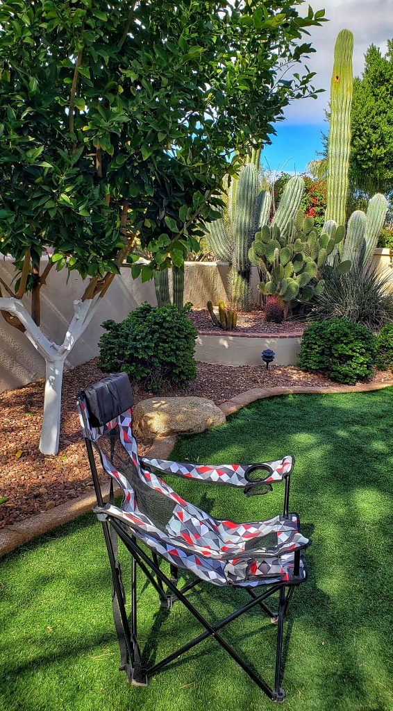 A photo of the folding chair Linda hauls around with her. I believe it folds back, but in this picture, it looks like a normal chair. The pattern is a bold print of gray and red triangles. Linda's cactus garden is visible in the background.