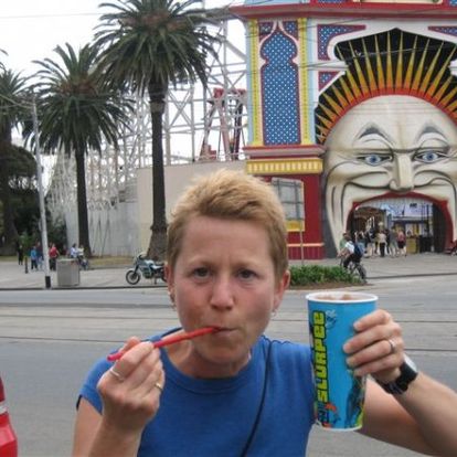 In this photo, Julie is sucking on a straw, and holding up her giant blue Slurpee cup. If the title is to be believed, it was taken in Luna Park, in Melbourne. Off in the distance to the left, a line of palm trees is visible. To the right, there is what looks to be the entrance to an amusement park.