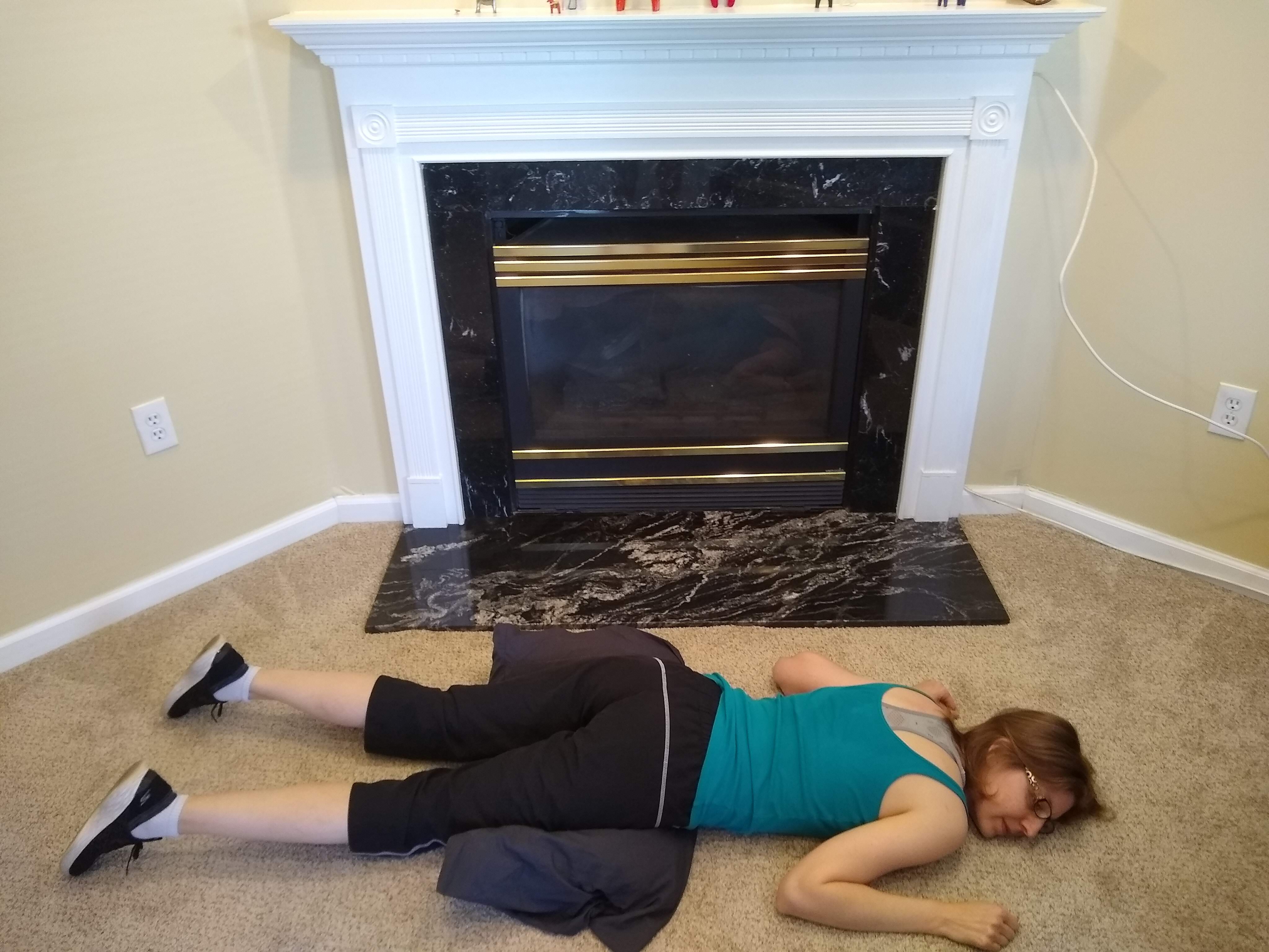 A photo of me lying face-down on the floor with a pillow under my hips. My head is tilted off to the right. There's a fireplace behind me. It's always cold in that room, but I never have been able to work that thing.