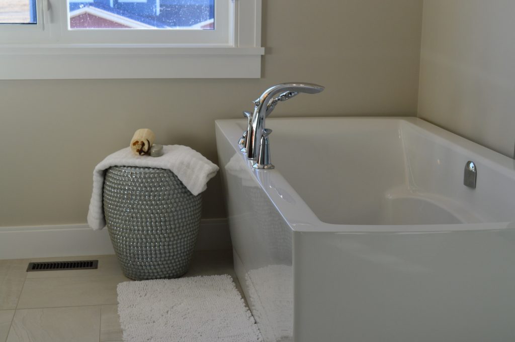 This photo shows a new bathtub tucked into the corner of a modern, clean bathroom. A basket and a bath mat are on the floor to the left of the bathtub. Otherwise, this is pretty much a picture of a normal bathtub. 