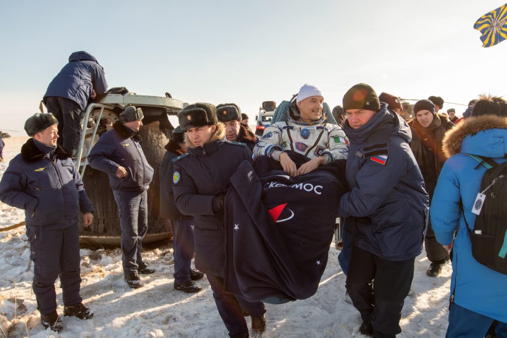 This photo shows ESA astronaut Luca Parmitano being carried in his seat liner after he returned from a six-month stint on the International Space Station. The ESA photo caption says he touched down in the Kazakh steppes, which would explain why there's snow on the ground, and many bystanders are wearing thick coats and fur hats. The scene does indeed look relatively crowded, and with the jam of people, it's hard to see what's going on in the background. Parmitano appears just right of center. He's still in his custom-molded seat, and is covered with a blanket. He's smiling, and looking off to his left. At least three people are carrying him, but there might be more. The angle of the photo makes it hard to tell.