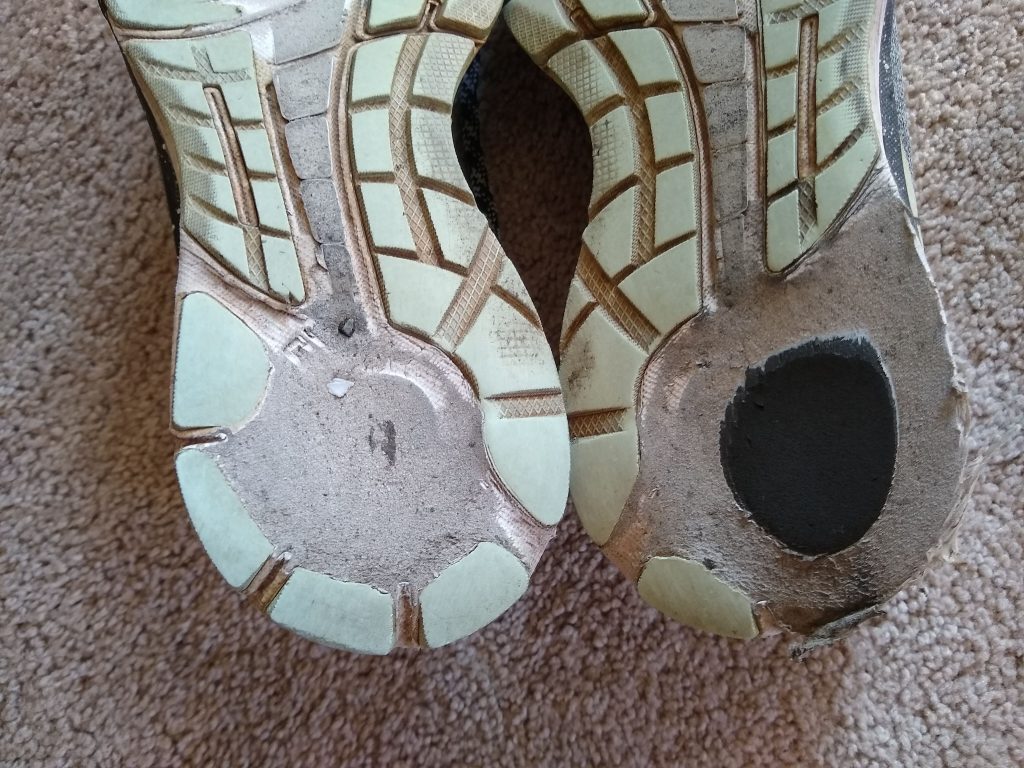 A photo of the bottom of my worn-out tennis shoes. The heel on right shoe is significantly worn, while the heel on the left shoe is practically gone.