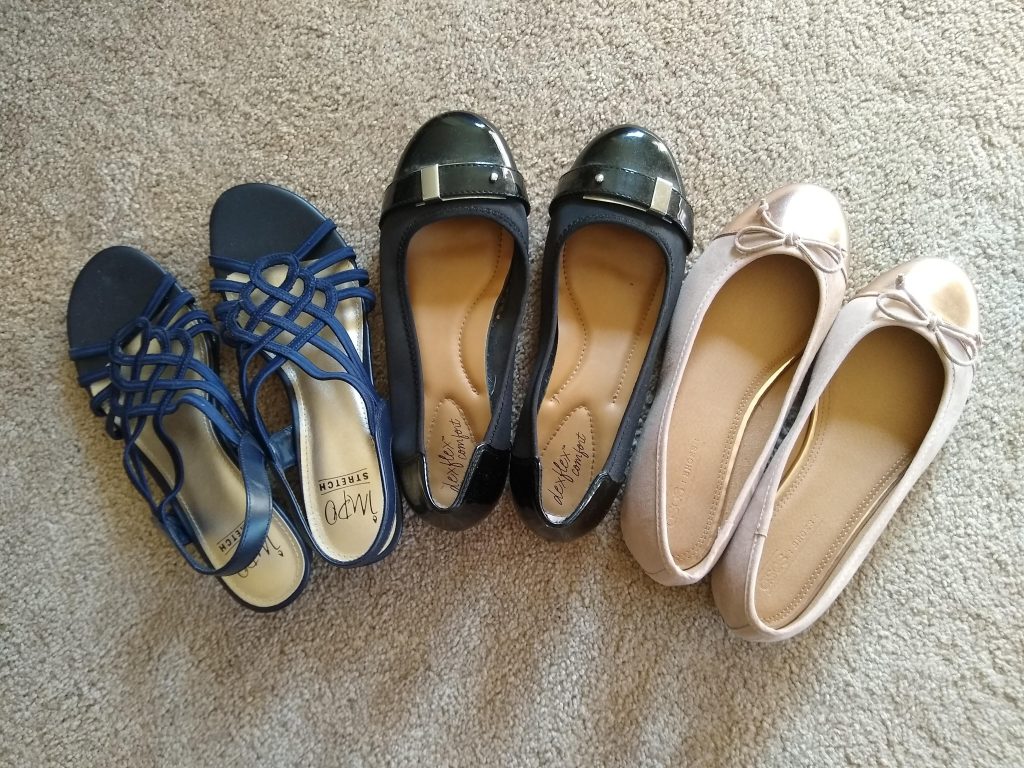 Three pairs of nice-ish shoes, arranged in an arc. On the left is a pair of navy blue strappy sandals with cushioned soles and low heels. On the right are two pairs of ballet flats, one black and one pink.