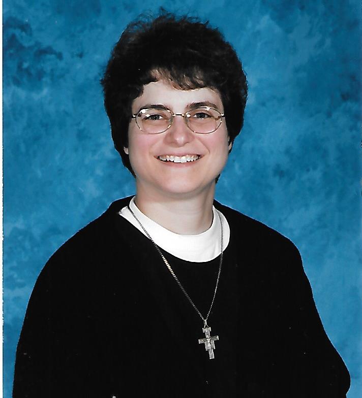 A photo of Maryanne as a novice. She's wearing a black habit and white collar. A silver crucifix is hanging around her neck. Her head is uncovered.