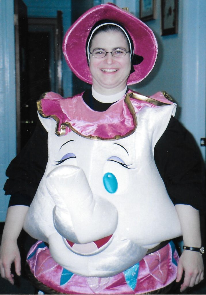 A photo of Maryanne from 2004. She's dressed in her full habit. On top of that, she's wearing a puffy, pink-and-white Mrs. Potts costume, based on the character from Beauty and the Beast.
