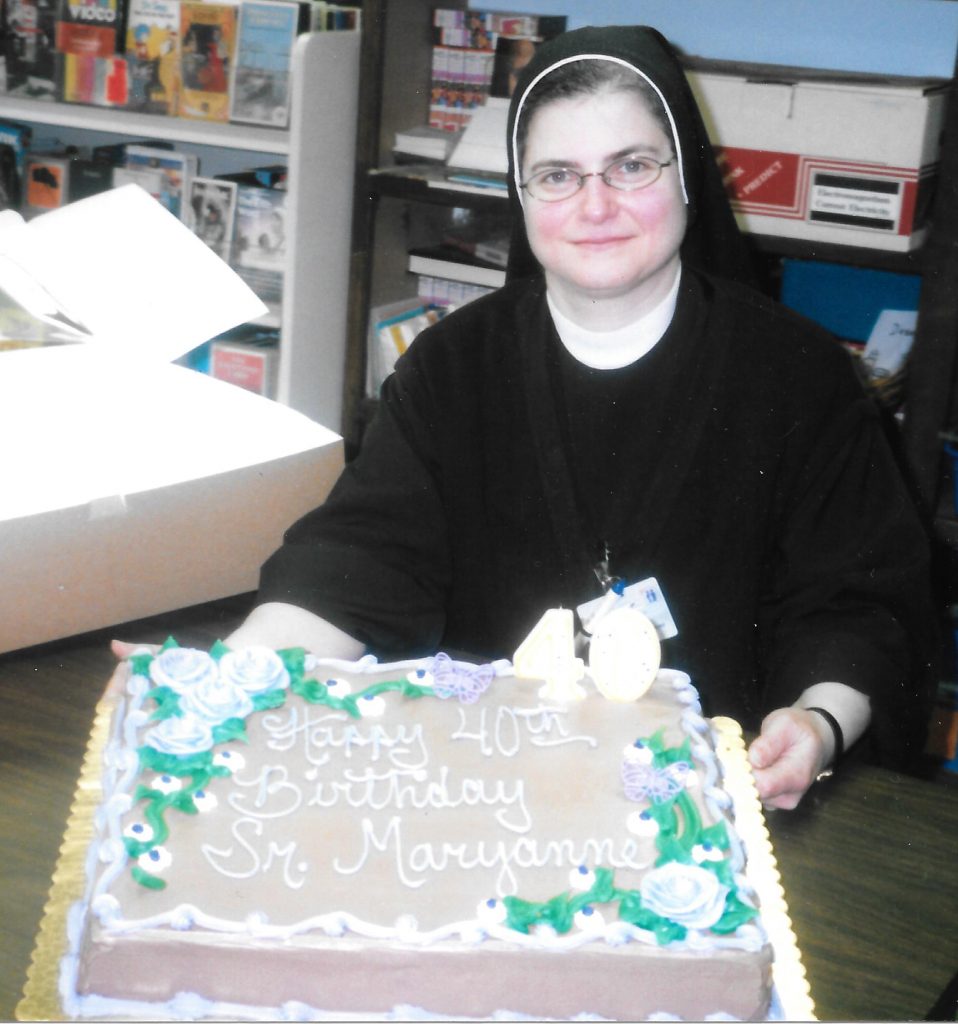 A photo of Maryanne taken a few months before she left the order. She's wearing her full black habit, and is sitting behind a table. She props up a cake with her hands. "Happy 40th Birthday Sr. Maryanne" is written in icing.