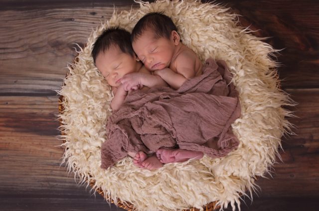 A photo of two, infant, male twins who are cuddling together under a brown blanket. They're laying on a fluffy white nest-thing. Below that is a wooden floor. I want to point out that I wanted to use a photo of adult, male, Finnish twins, but good luck finding a free-to-reuse photo of that.